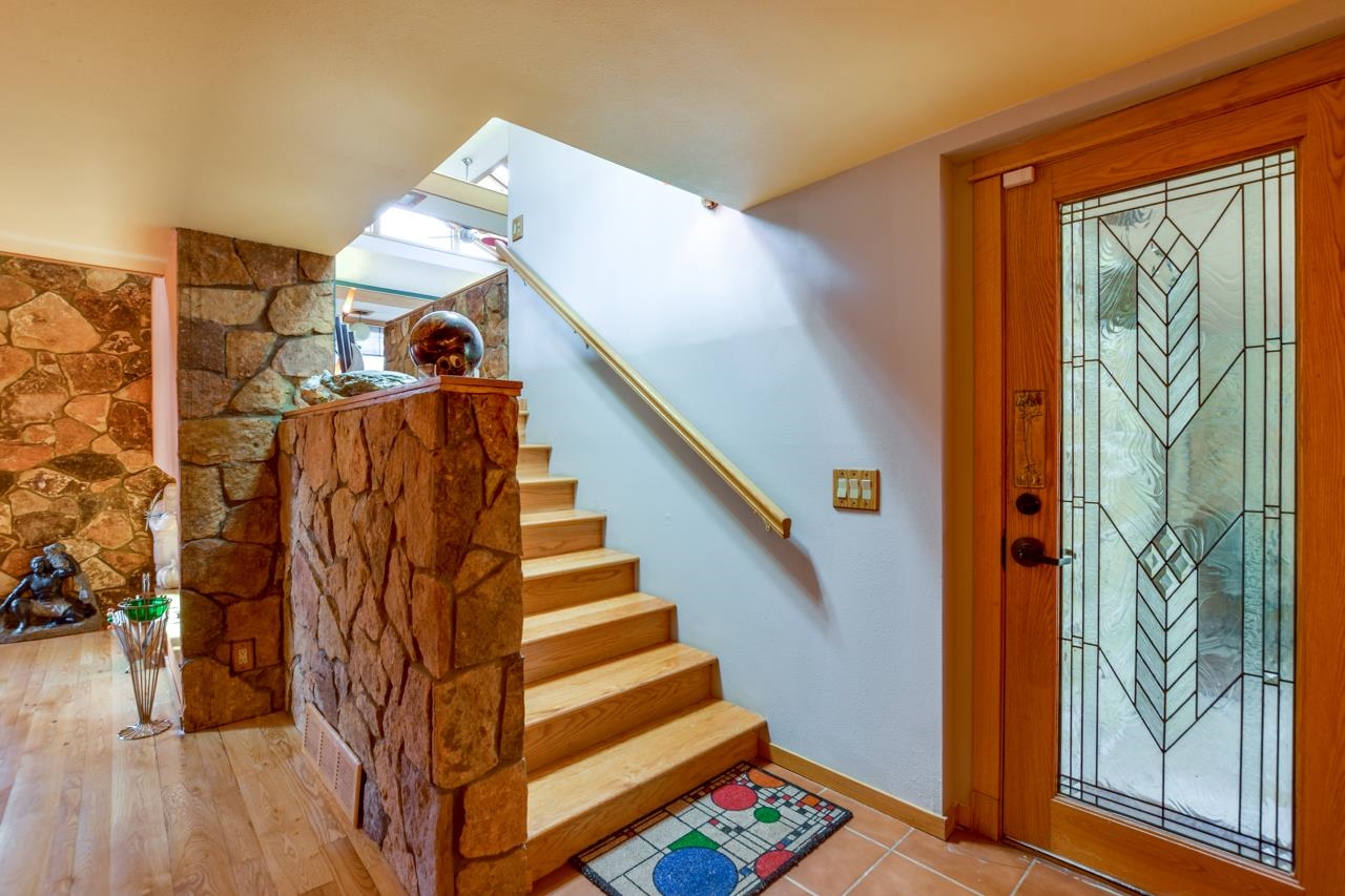 Entryway with wooden stairs, a stone half-wall, and a decorative leaded-glass front door.