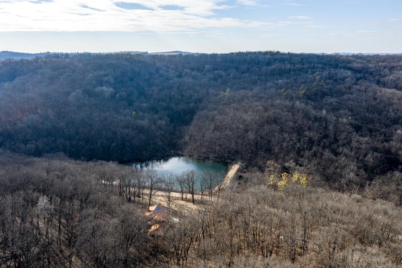 Aerial view of a wooded property with a pond and a partly obscured house.