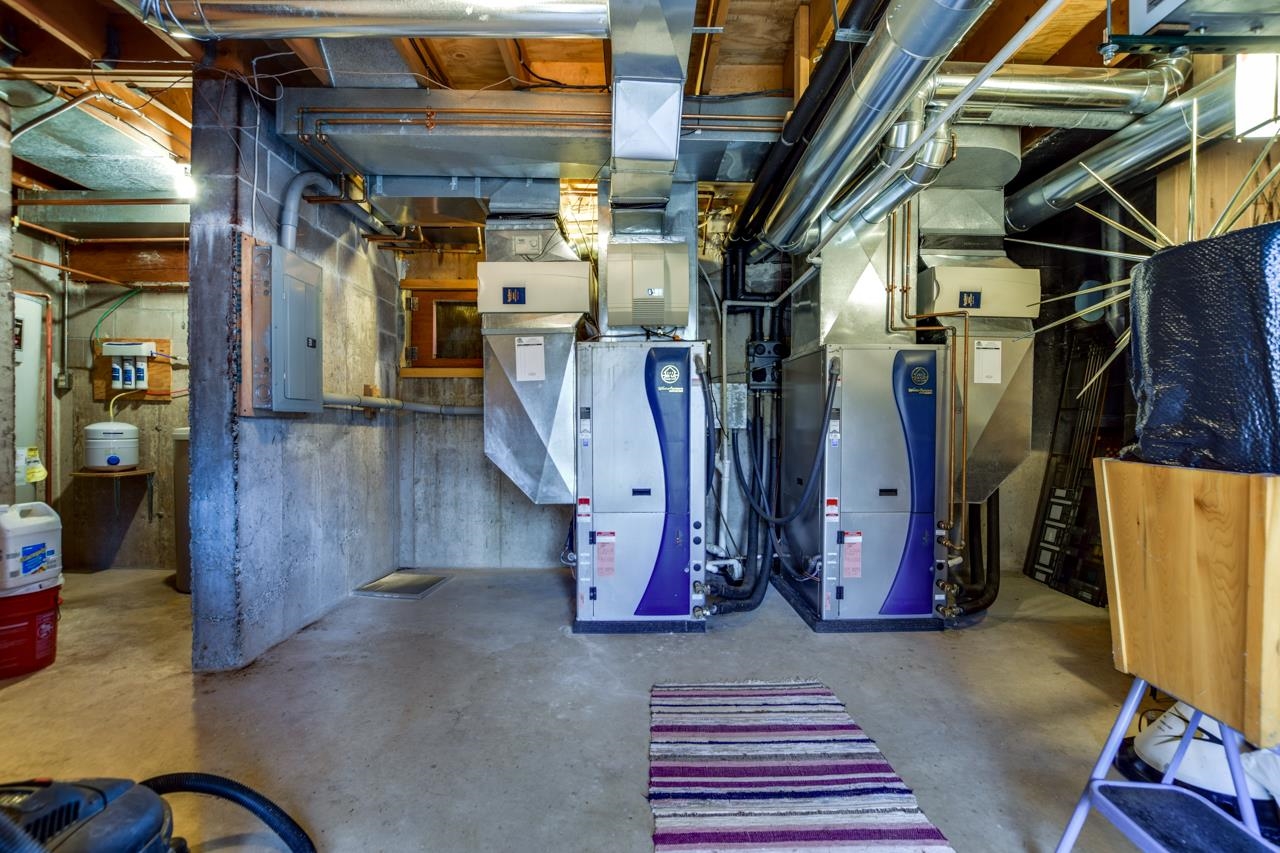 Basement mechanical room with two heating units and exposed ductwork above a concrete floor.