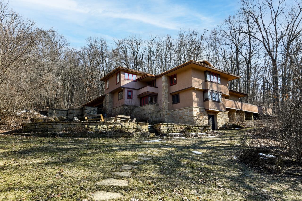 Multilevel stucco and stone home with a low stone terrace in a leafless woodland.