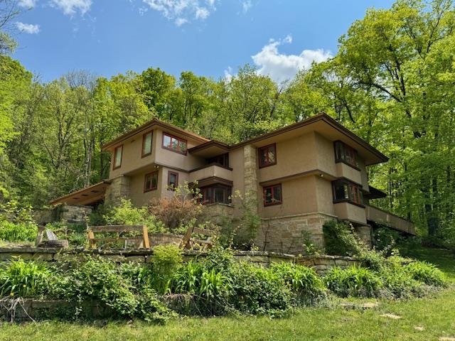 Two-story tan stucco home with stone accents, a garden, and leafy trees.