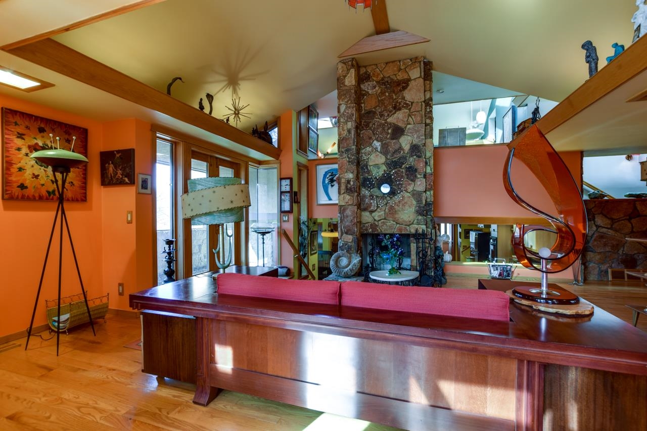 Living room with a tall stone fireplace, vaulted ceiling, and sculptural glass furnishings.