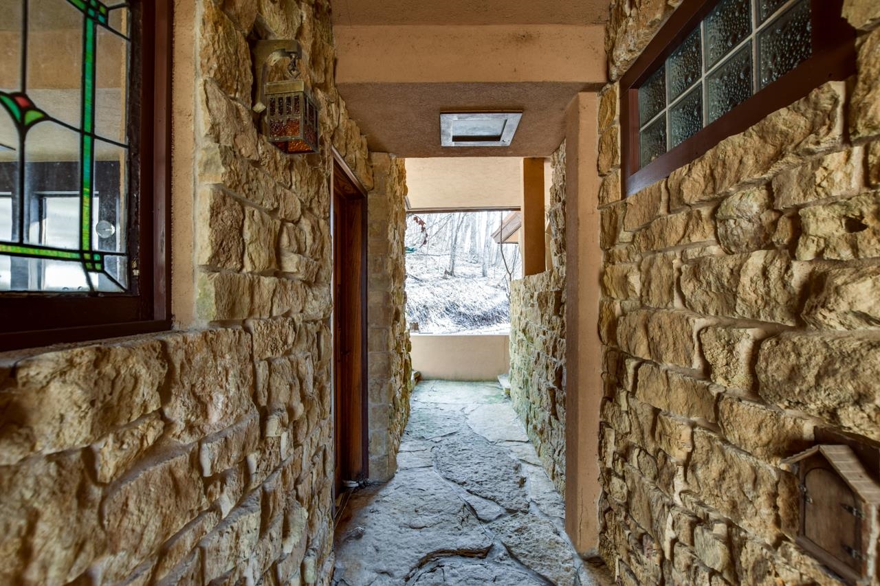 Stone entry passage with a flagstone floor, stained-glass window, and snowy woods beyond.