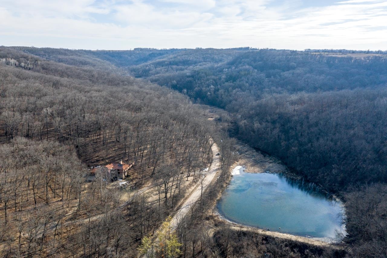 Wooded hills, a small cabin, winding driveway, and pond seen from above.