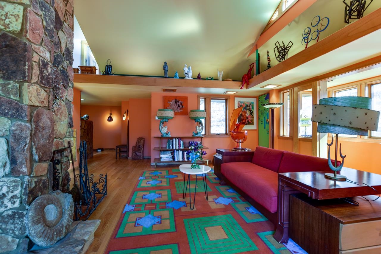 Living room with a stone fireplace, red sofa, and colorful geometric rug.