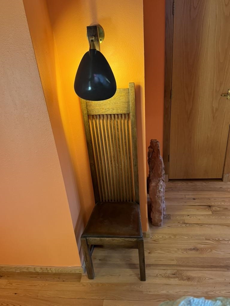 Wooden slat-back chair beneath a black wall lamp in an orange-walled interior nook.