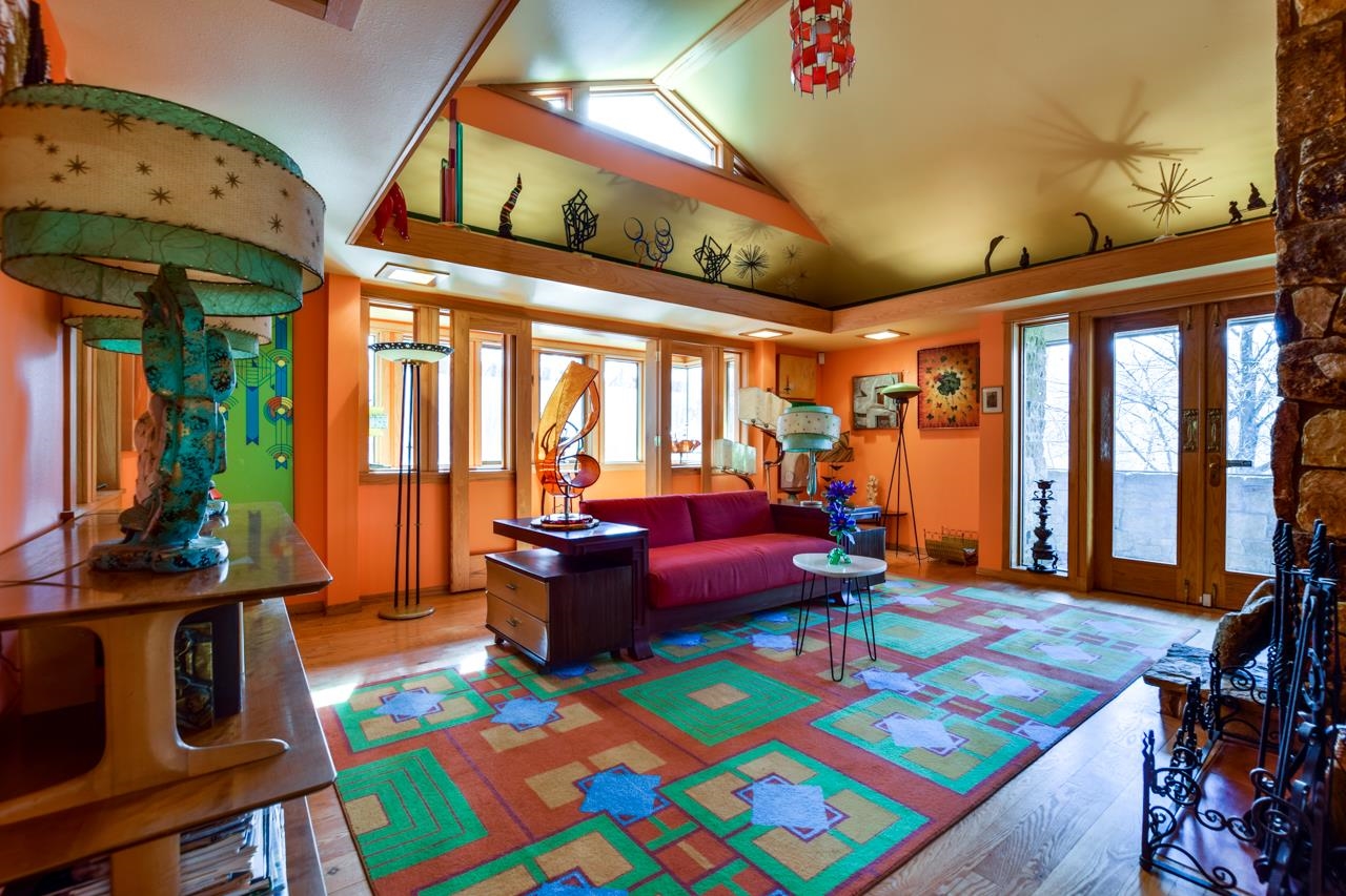 Furnished living room with vaulted ceiling, colorful geometric rug, and large windows.