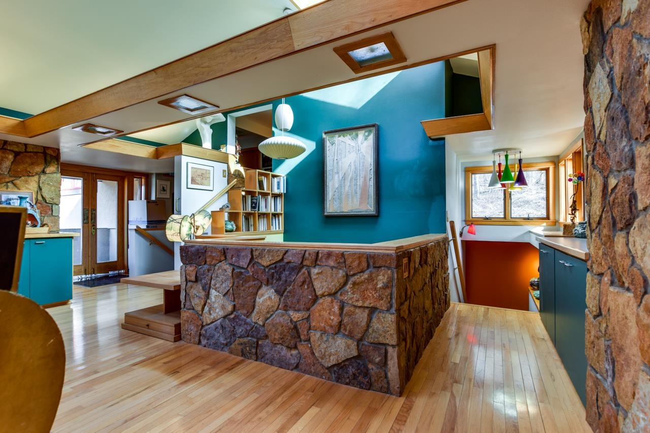 Open-plan kitchen with turquoise walls, hardwood floors, and a stone half-wall beneath exposed wood beams.