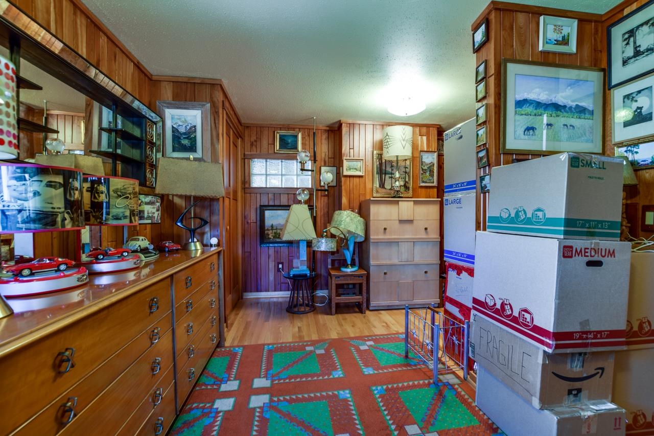 Wood-paneled room with collectible displays, model cars, a colorful rug, and stacked moving boxes.