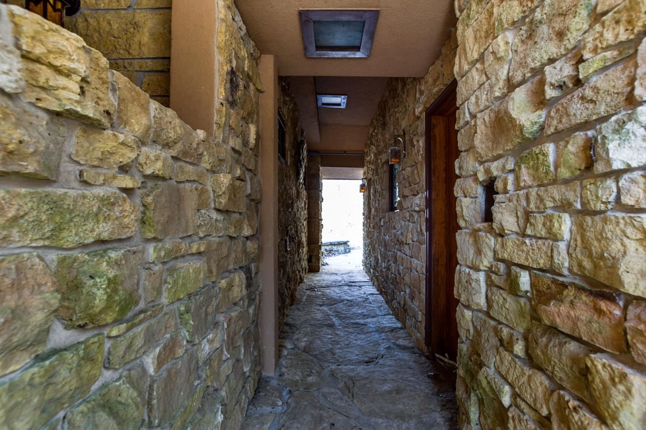 Stone hallway with a flagstone floor, wall lanterns, and a bright doorway at the far end.