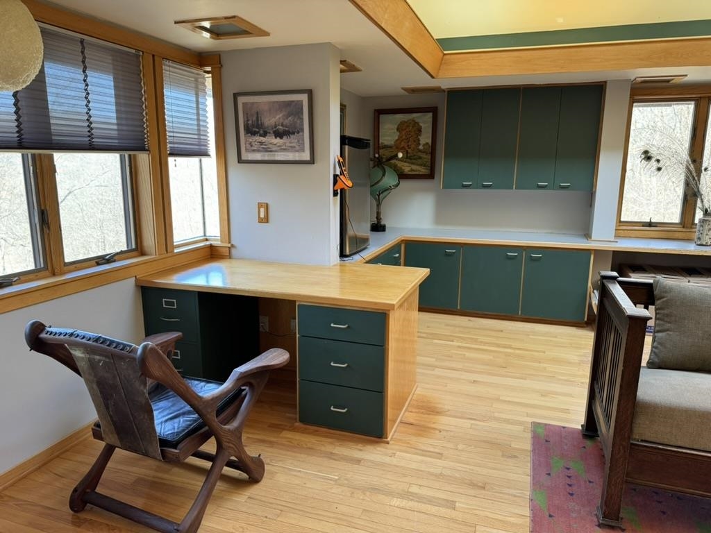 Home office with teal built-ins, a wood-topped desk, hardwood floors, and large windows.