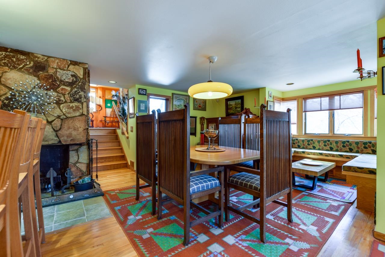 Dining room with a stone fireplace, tall wood chairs, and a colorful geometric rug.