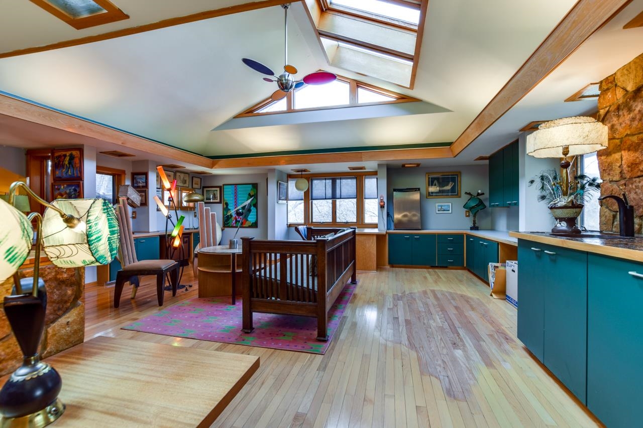 Open-plan kitchen and living area with teal cabinets, skylights, and a stone fireplace.