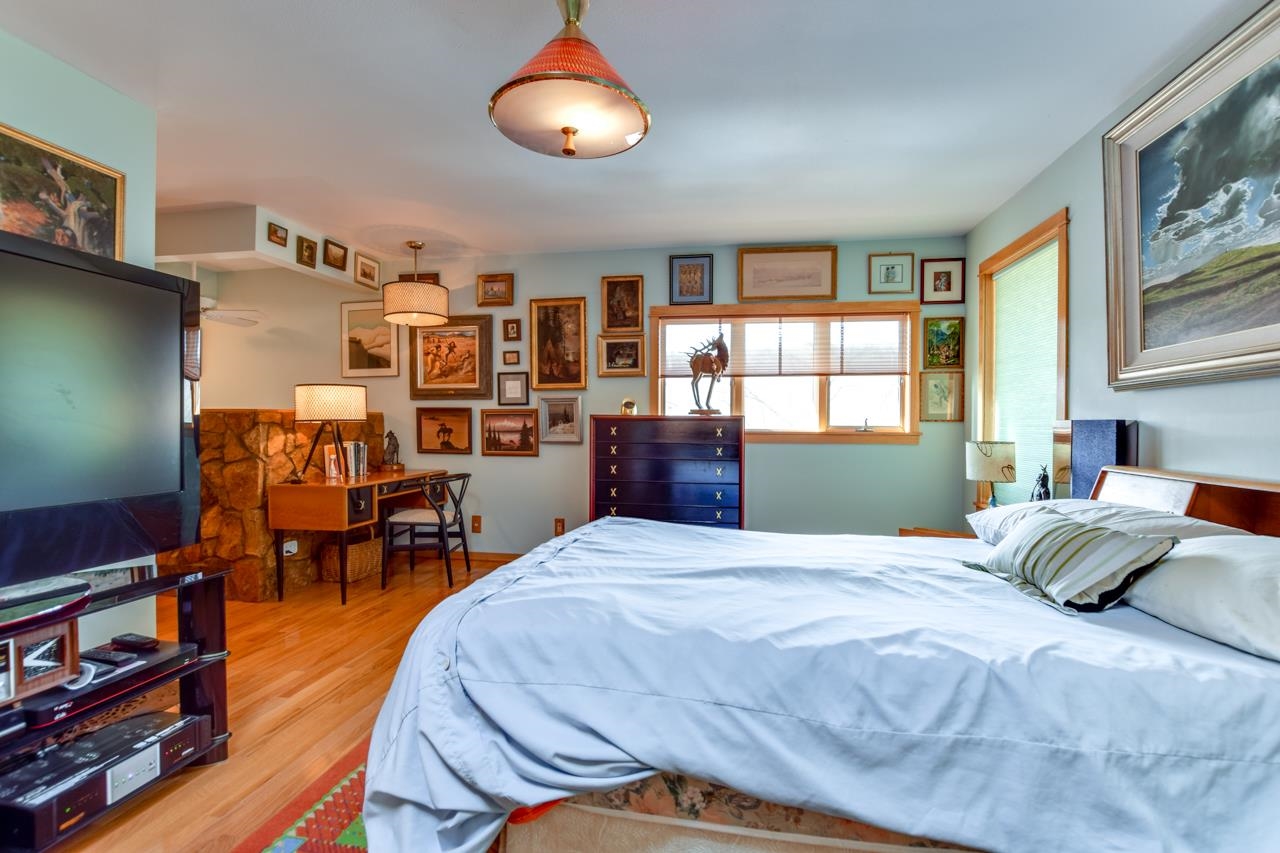 Bedroom with a large bed, stone fireplace, wood floors, and walls covered in framed pictures.