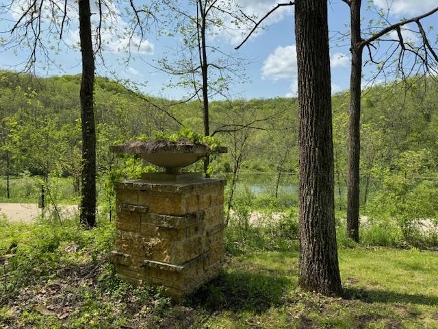 Stone fountain among trees, with a creek visible in the background.