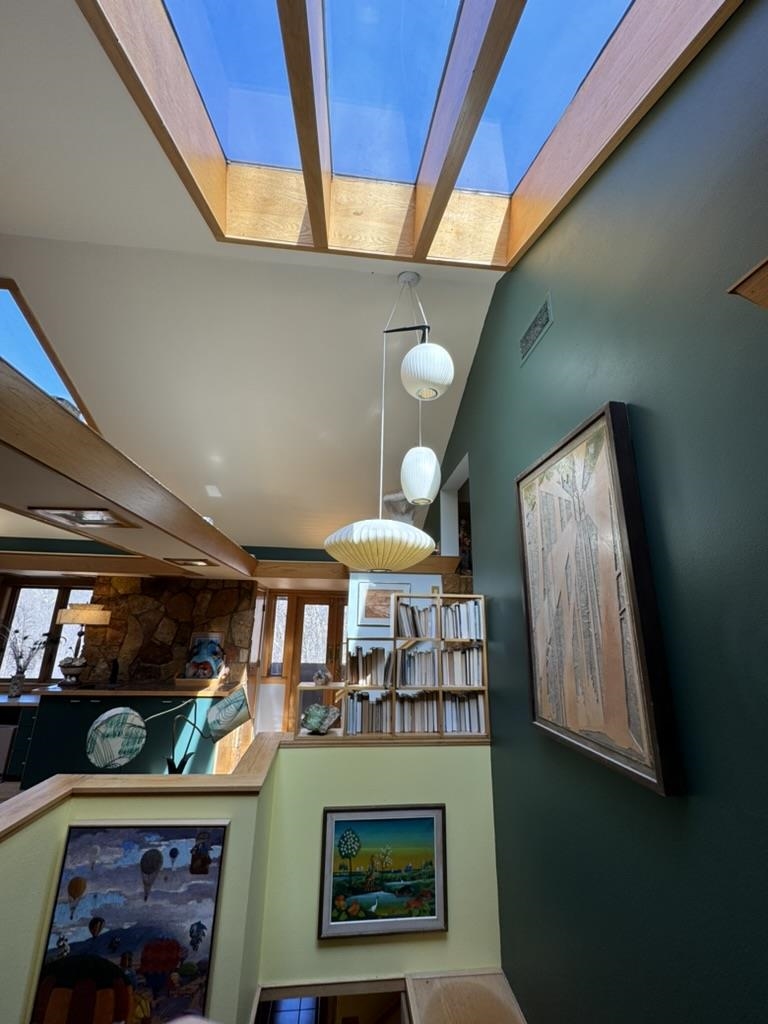 Tall interior with wood-framed skylights, pendant lights, built-in bookshelves, and a stone fireplace wall.
