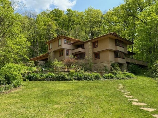 Multi-level house among trees, with a broad lawn and stepping-stone path.