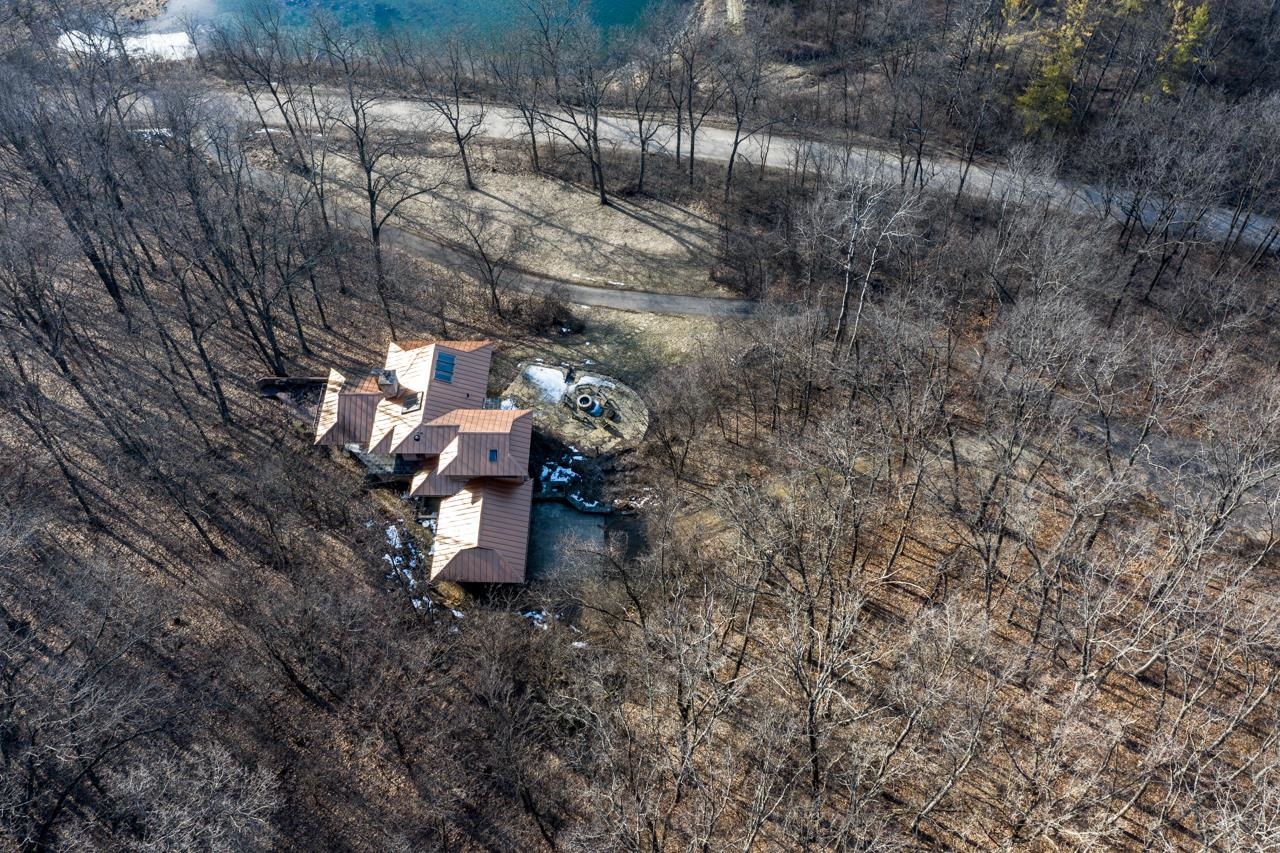 Aerial view of a copper-roofed home among leafless trees, with a winding driveway and water feature.
