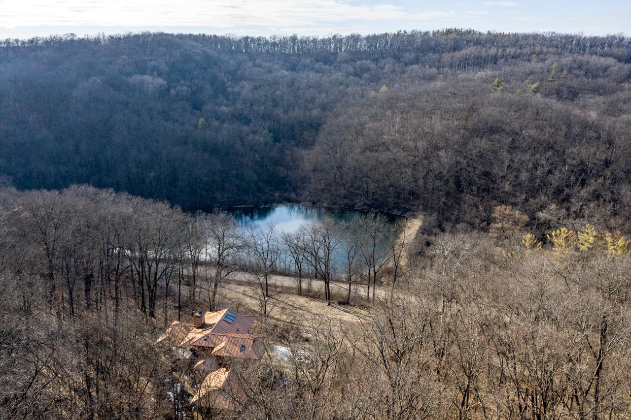 A home among leafless woodland overlooks a pond and wooded hills.