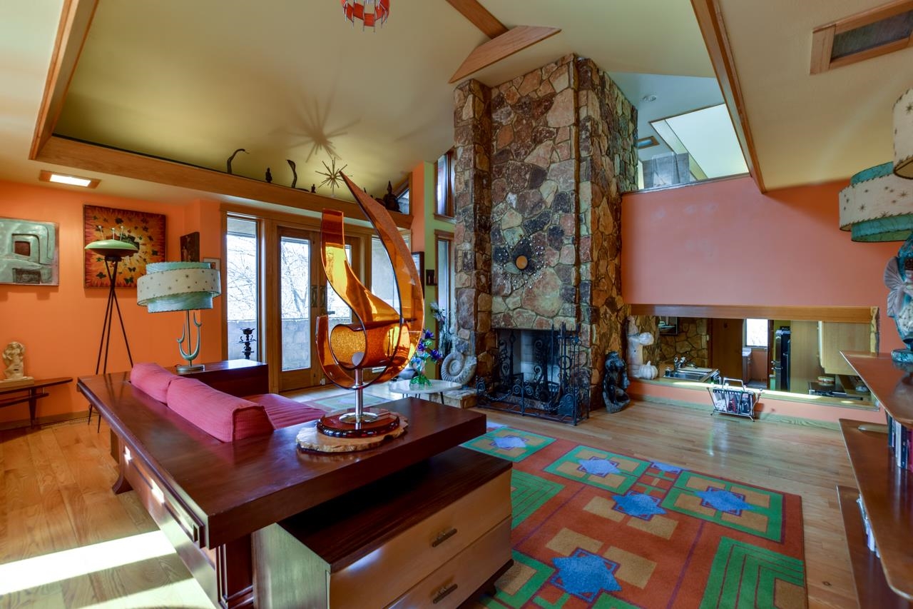 Living room with a tall stone fireplace, sculptural hanging chair, and colorful geometric rug.