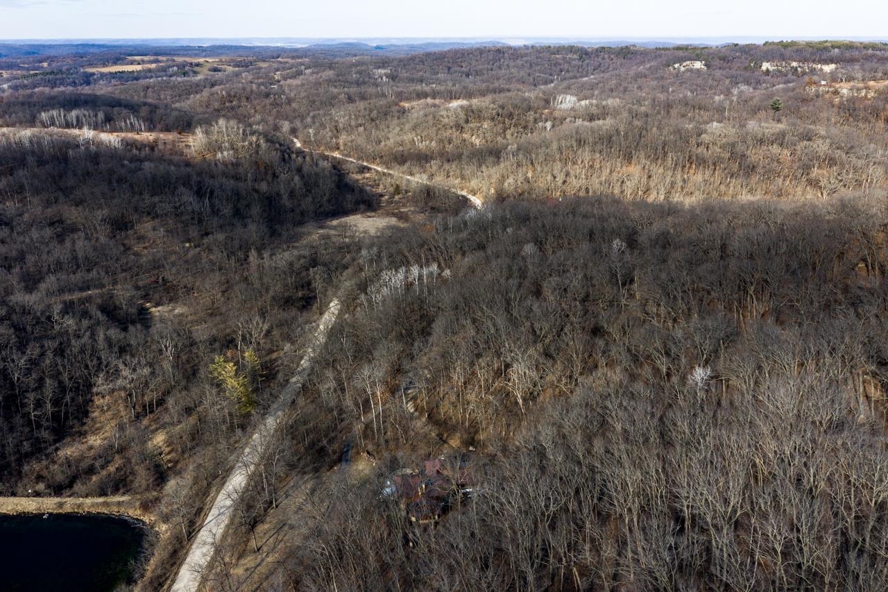 Aerial view of wooded acreage with a winding driveway and small pond.