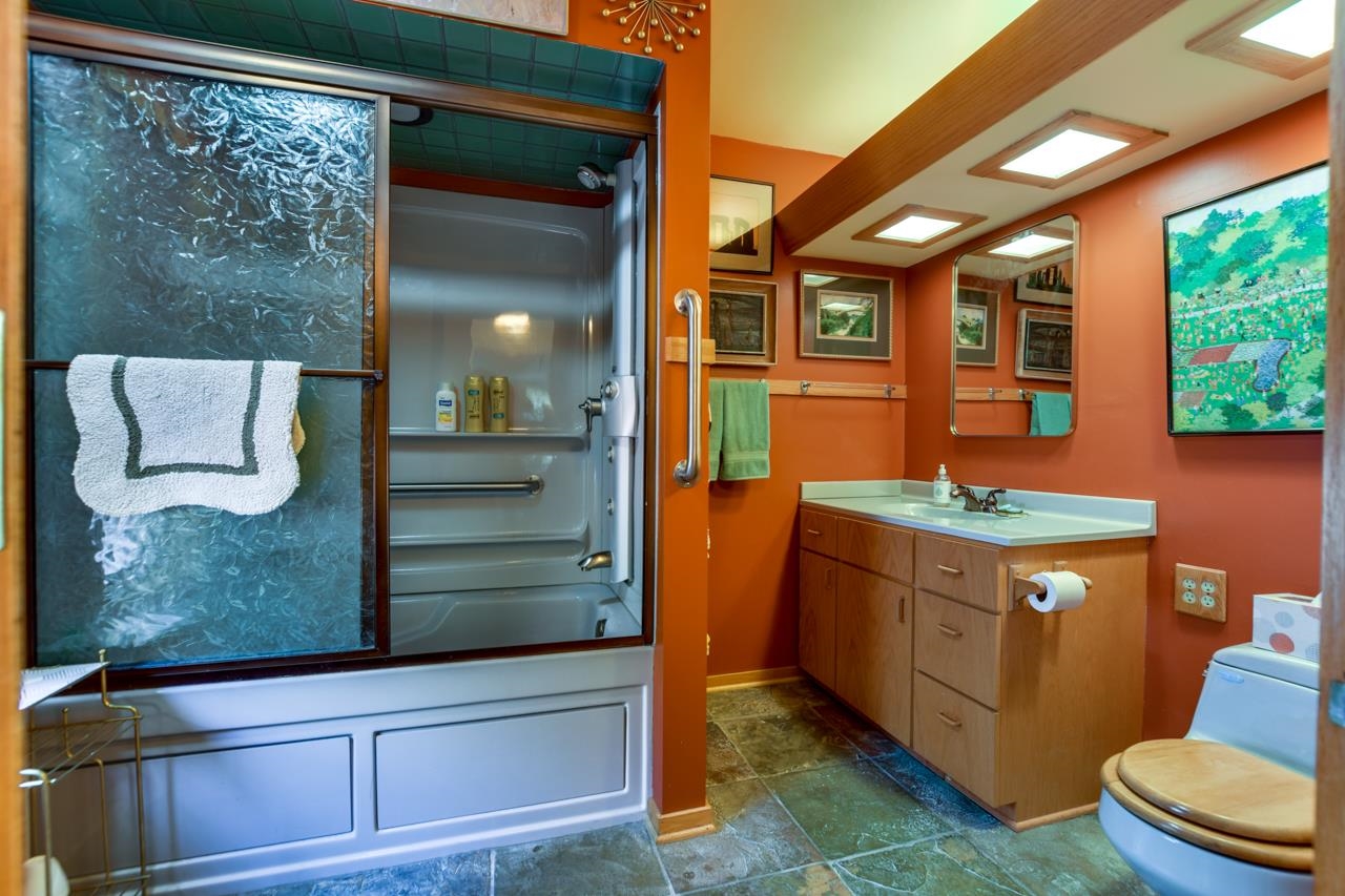 Bathroom with a glass-enclosed shower, wood vanity, orange walls, and framed artwork.