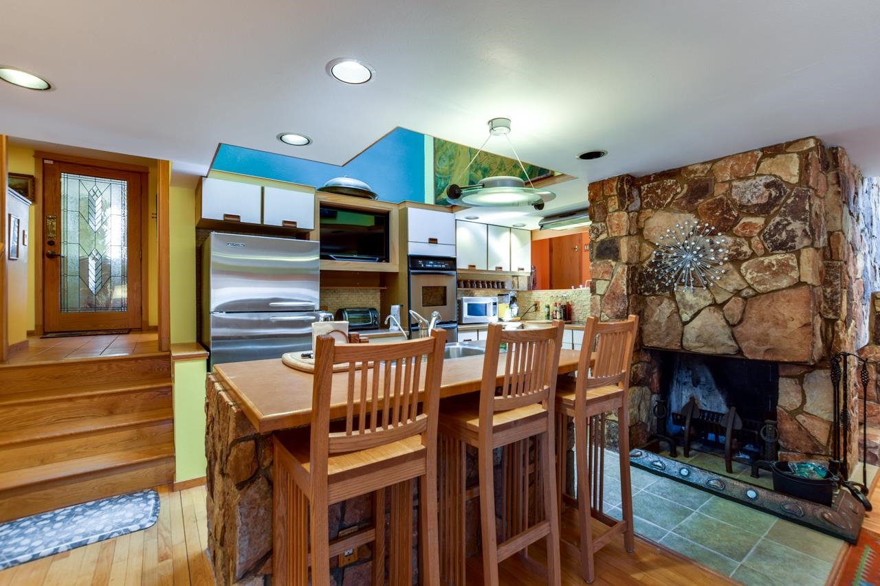 Kitchen and dining area with a stone fireplace, stainless steel appliances, and a wood breakfast bar.