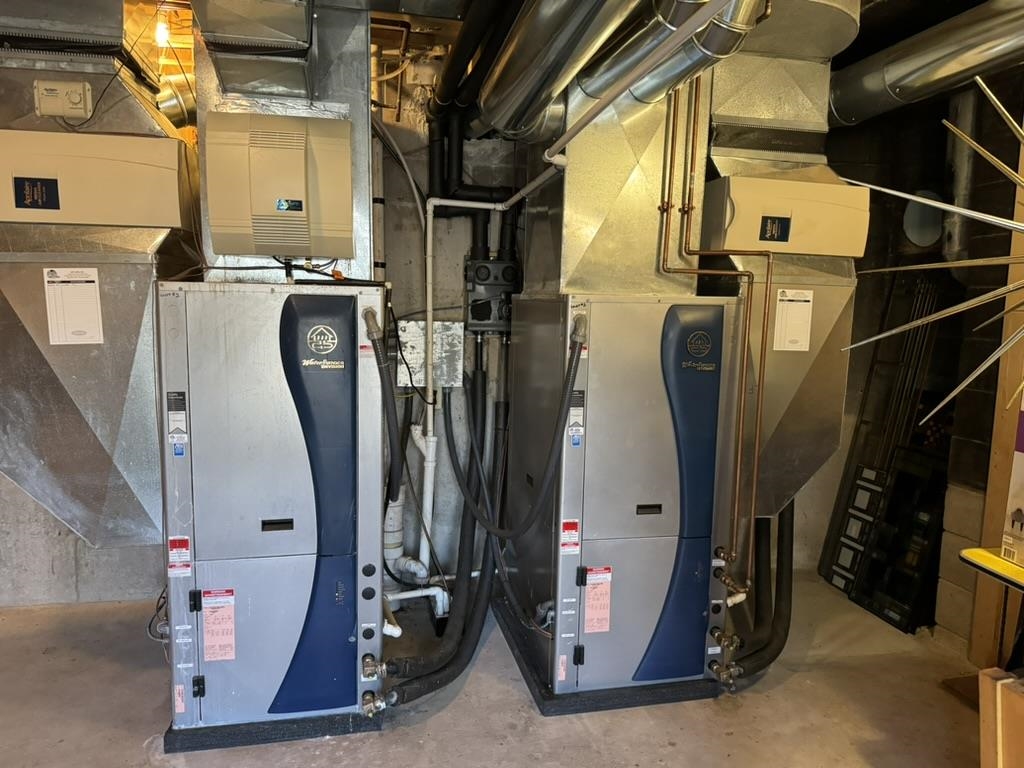 Utility room with two large geothermal heating and cooling units and exposed ductwork.