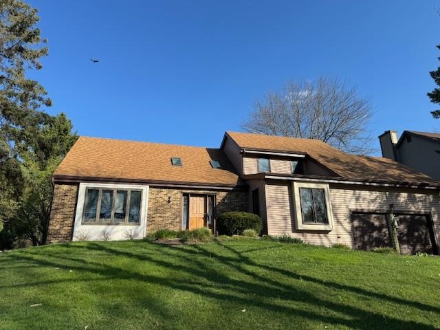 Home with brick and siding, tan roof, attached garage, and sloping lawn.