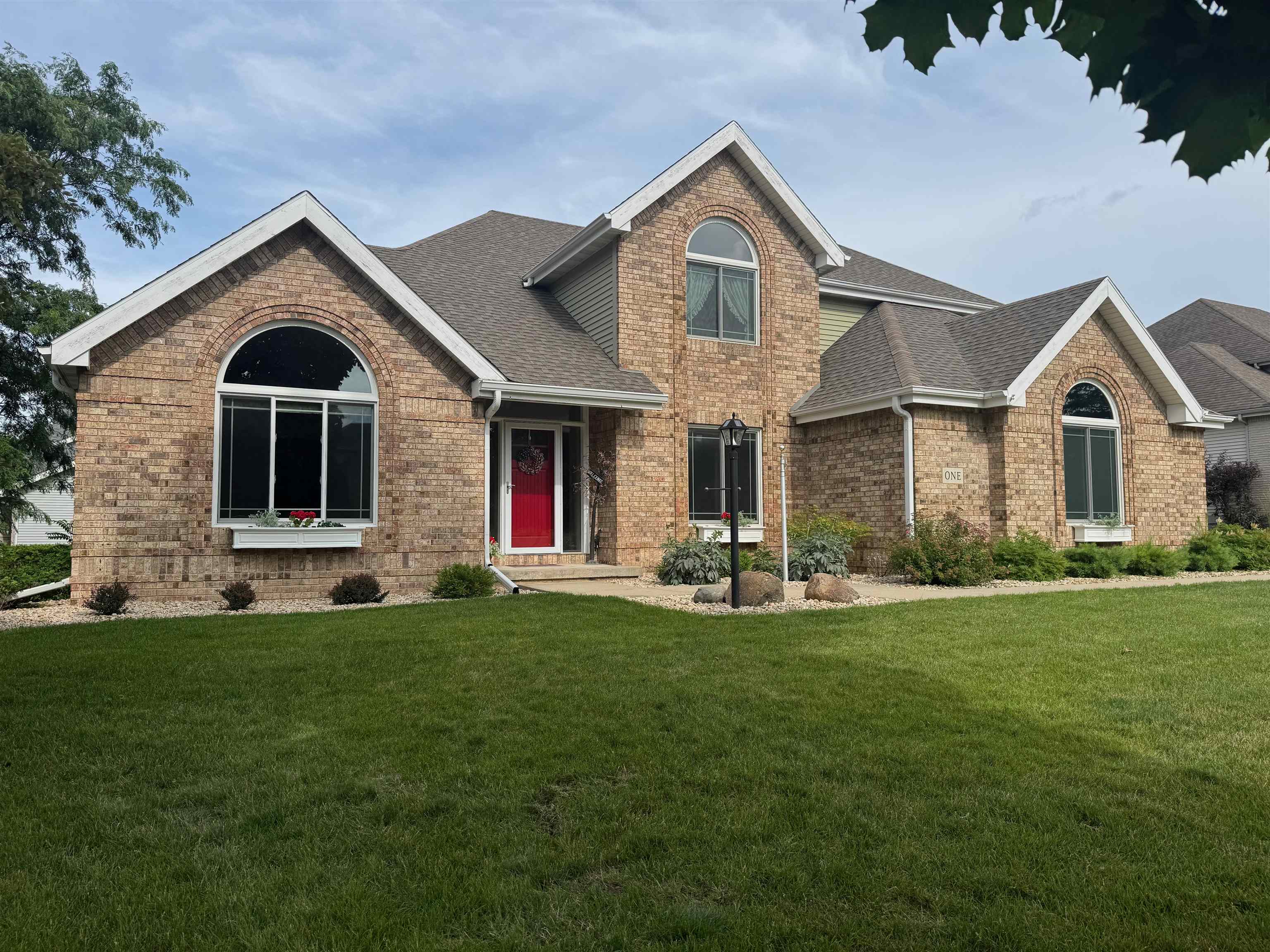 Two-story tan brick house with arched windows, a red front door, and a broad lawn.