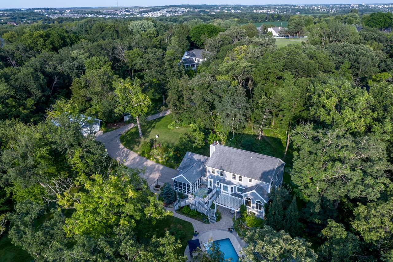Aerial view of a gray two-story house among trees, with a deck and backyard pool.