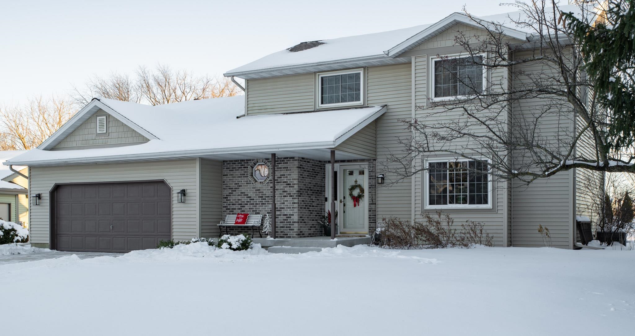 Two-story gray house with a brick entry and double garage, surrounded by snow.