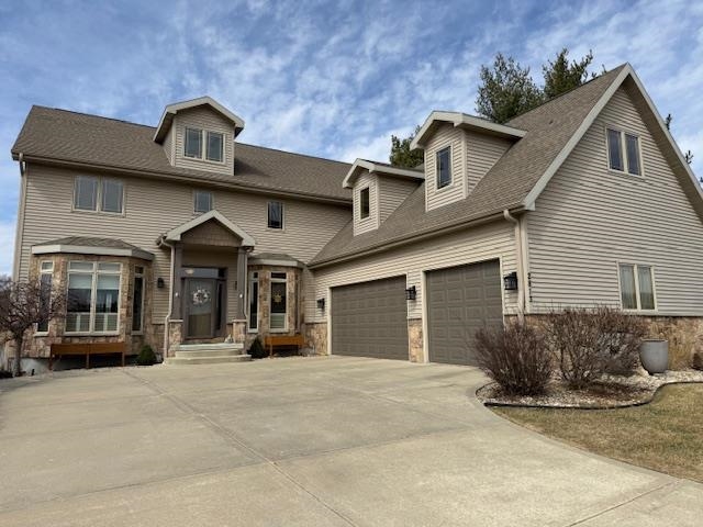 Two-story beige home with stone accents, multiple dormers, and a broad driveway.