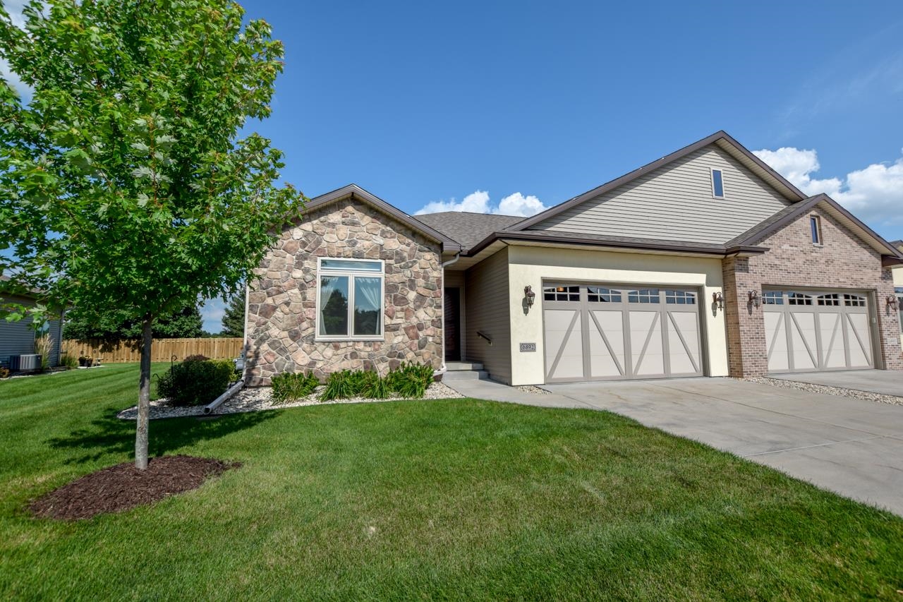 Home exterior with stone and brick accents, double garage doors, and a mature tree in the front lawn.