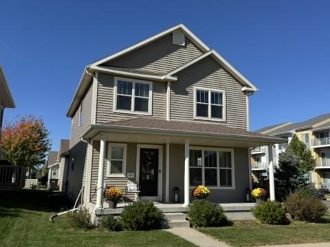 Two-story gray house with a covered porch, flower beds, and a front lawn.