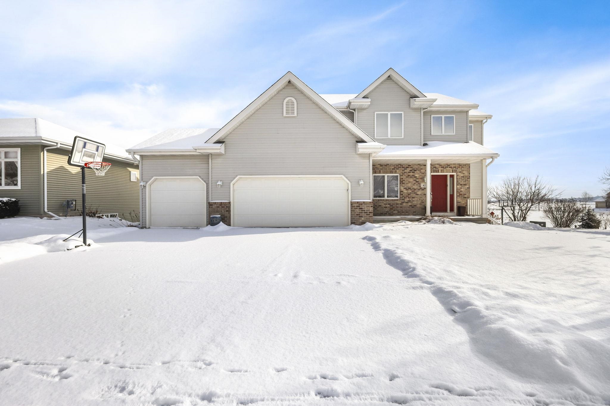 Two-story gray house with a brick entry and red door, surrounded by snow.