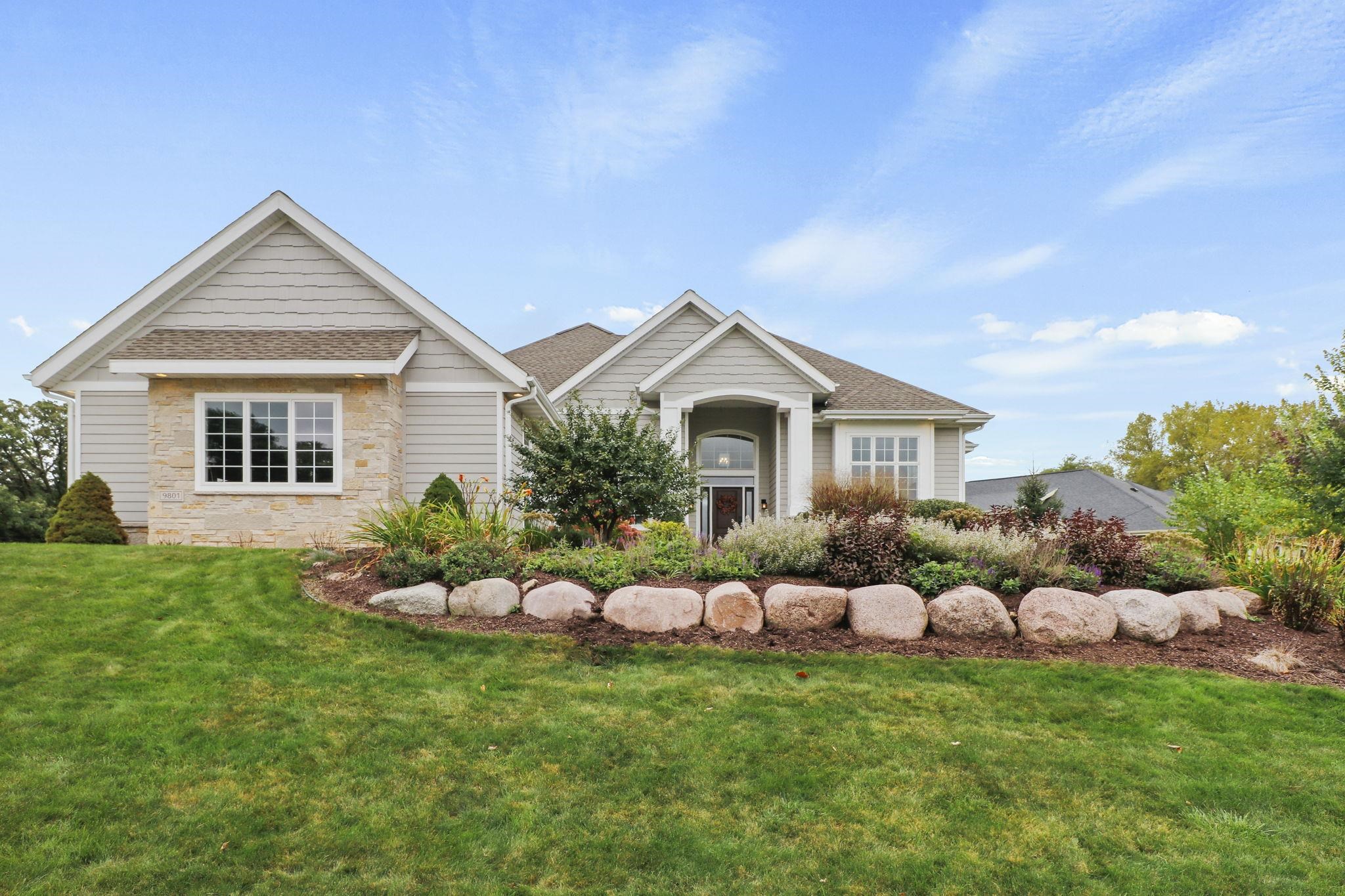 Home exterior with stone accents, a covered entry, and landscaped beds edged with large boulders.