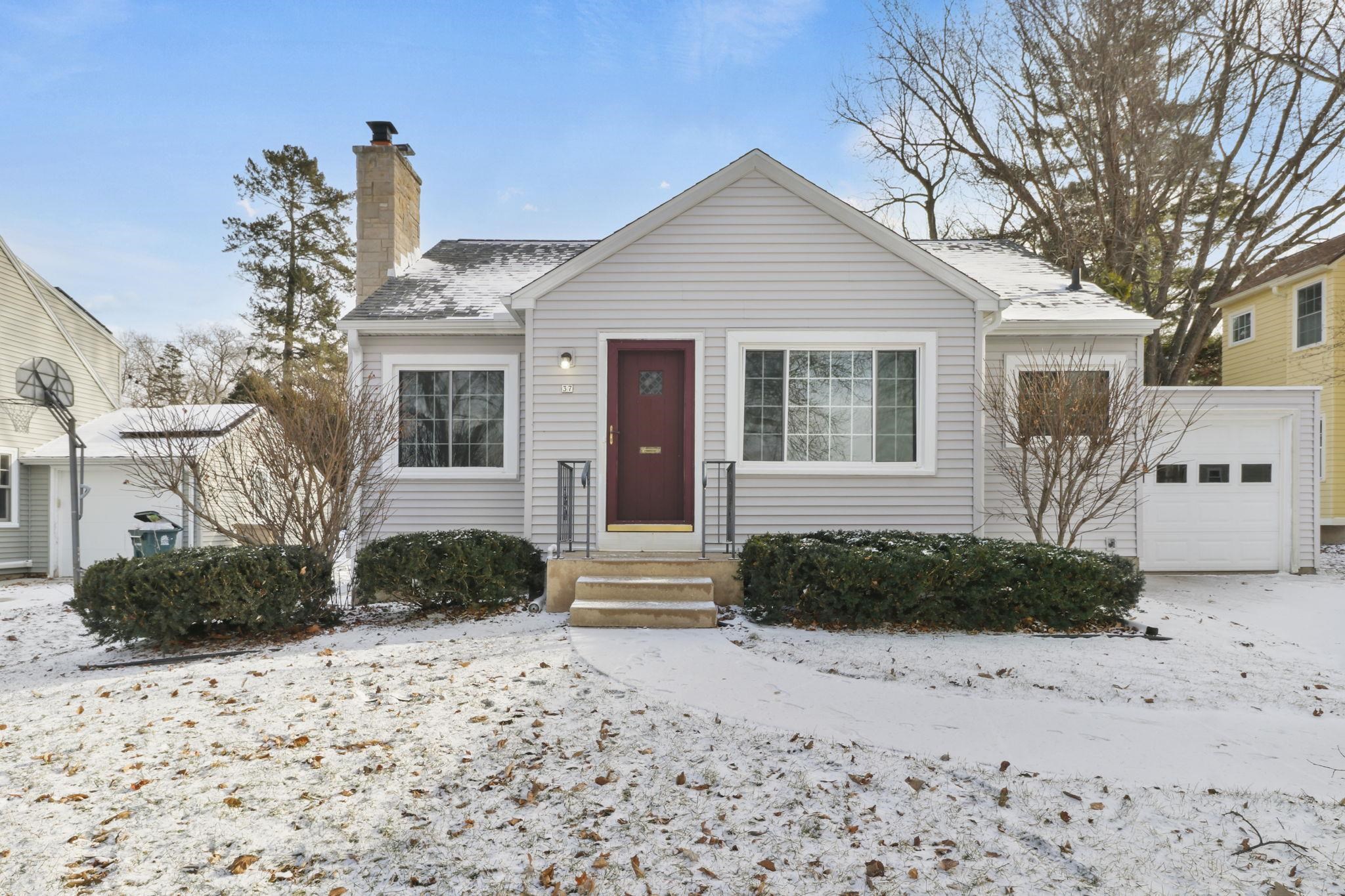 White-sided house with a red front door, stone chimney, and attached garage in winter.