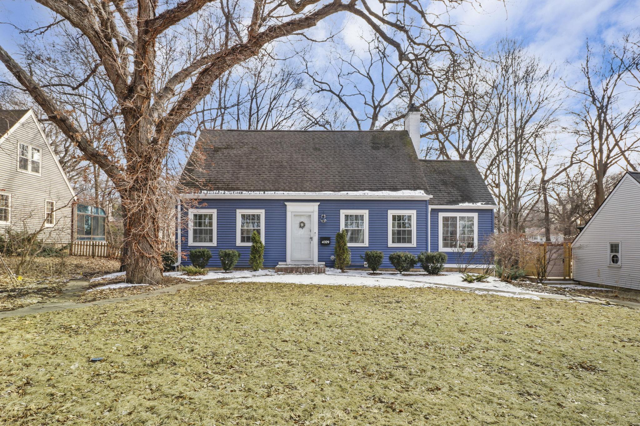 Blue house with white trim and a large bare tree in the snowy front yard.