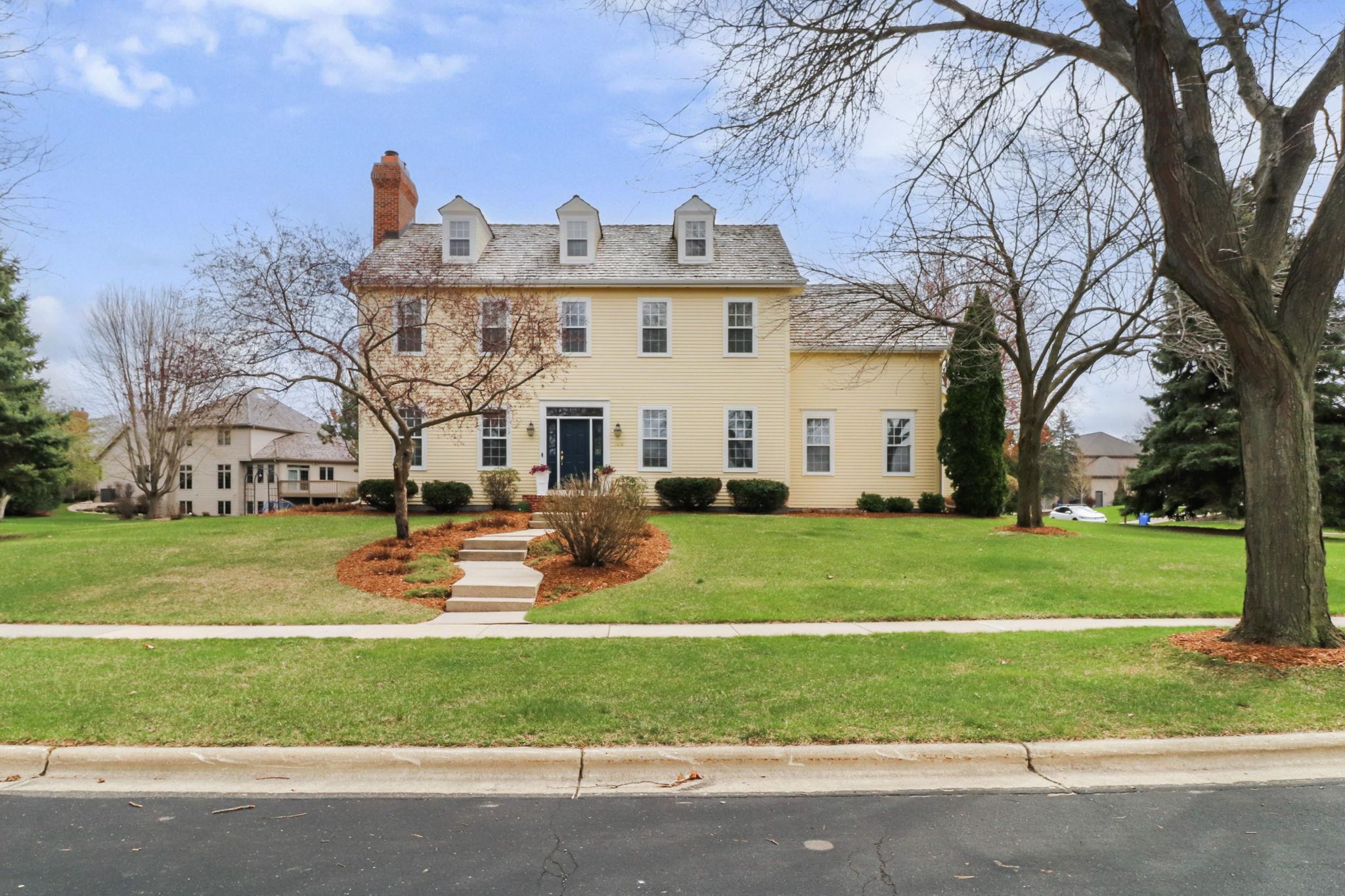 Yellow two-story home with three roof dormers, a brick chimney, and a landscaped front lawn.