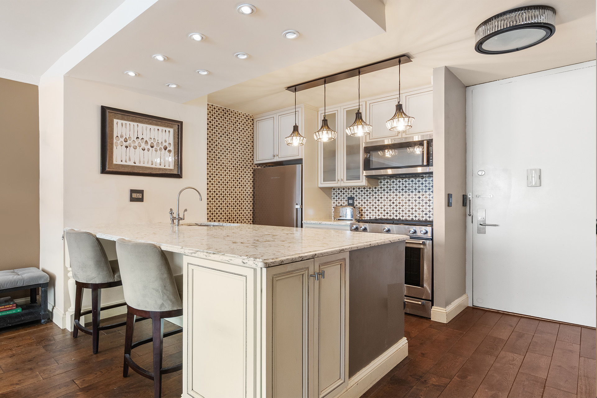 Kitchen with a marble-topped island, pendant lights, patterned backsplash, and stainless steel appliances.