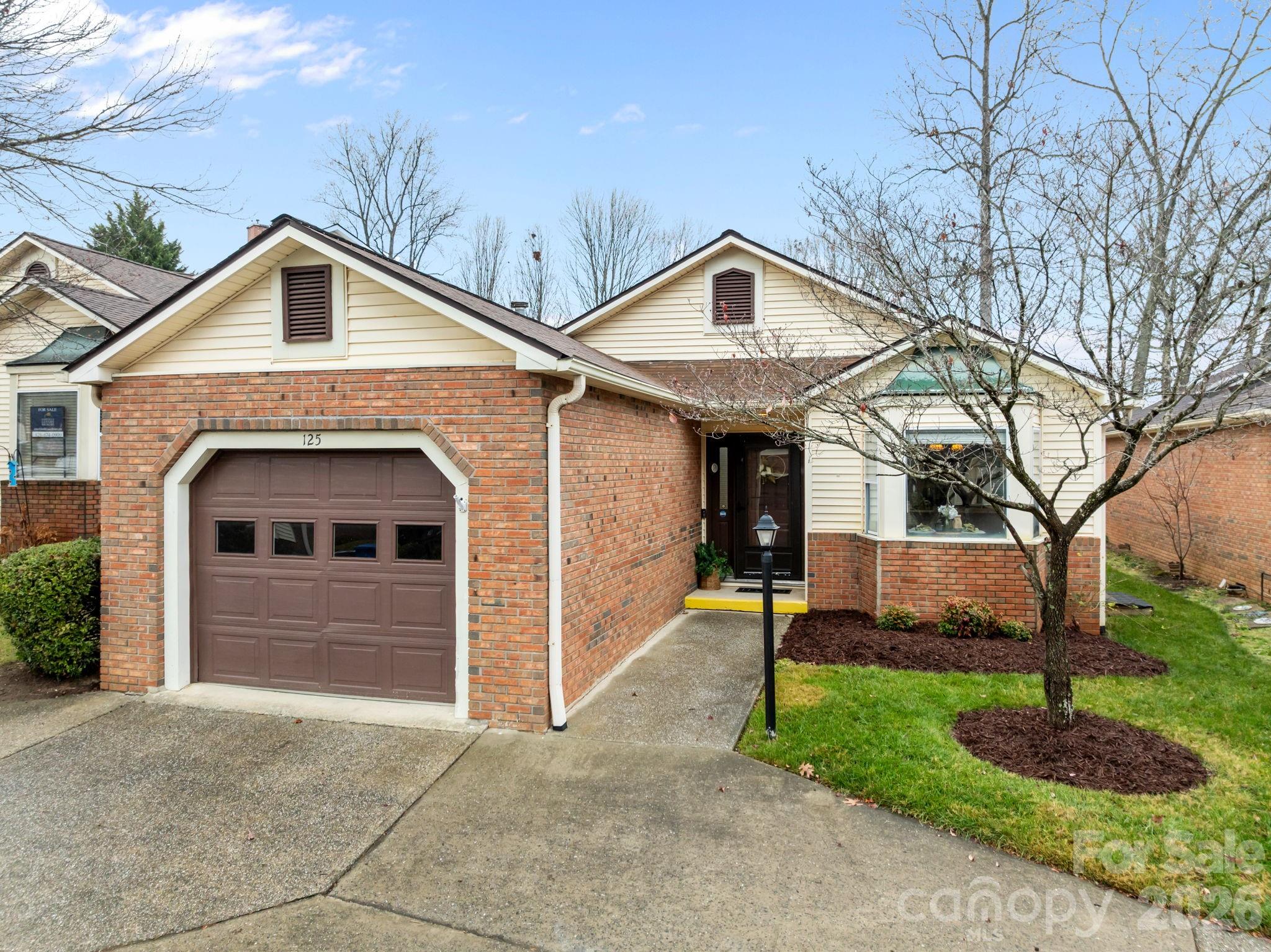Brick-and-siding house with a brown garage, recessed entry, and leafless front-yard tree.