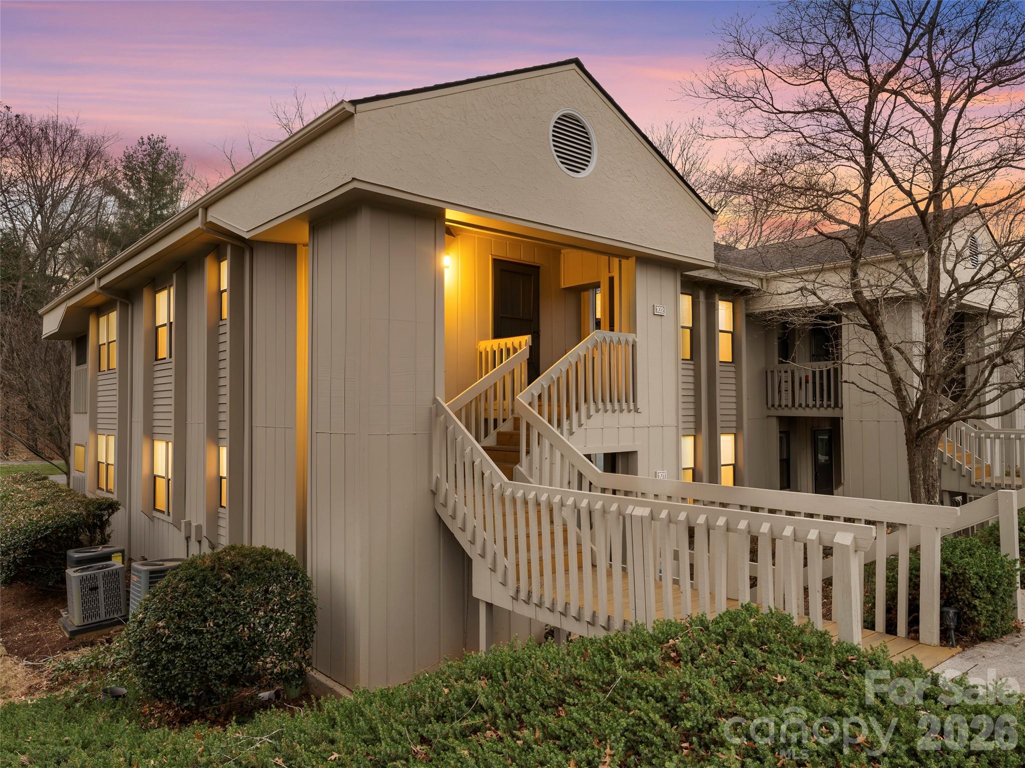 Beige multi-unit building with a raised entrance, illuminated windows, and wooden walkways.