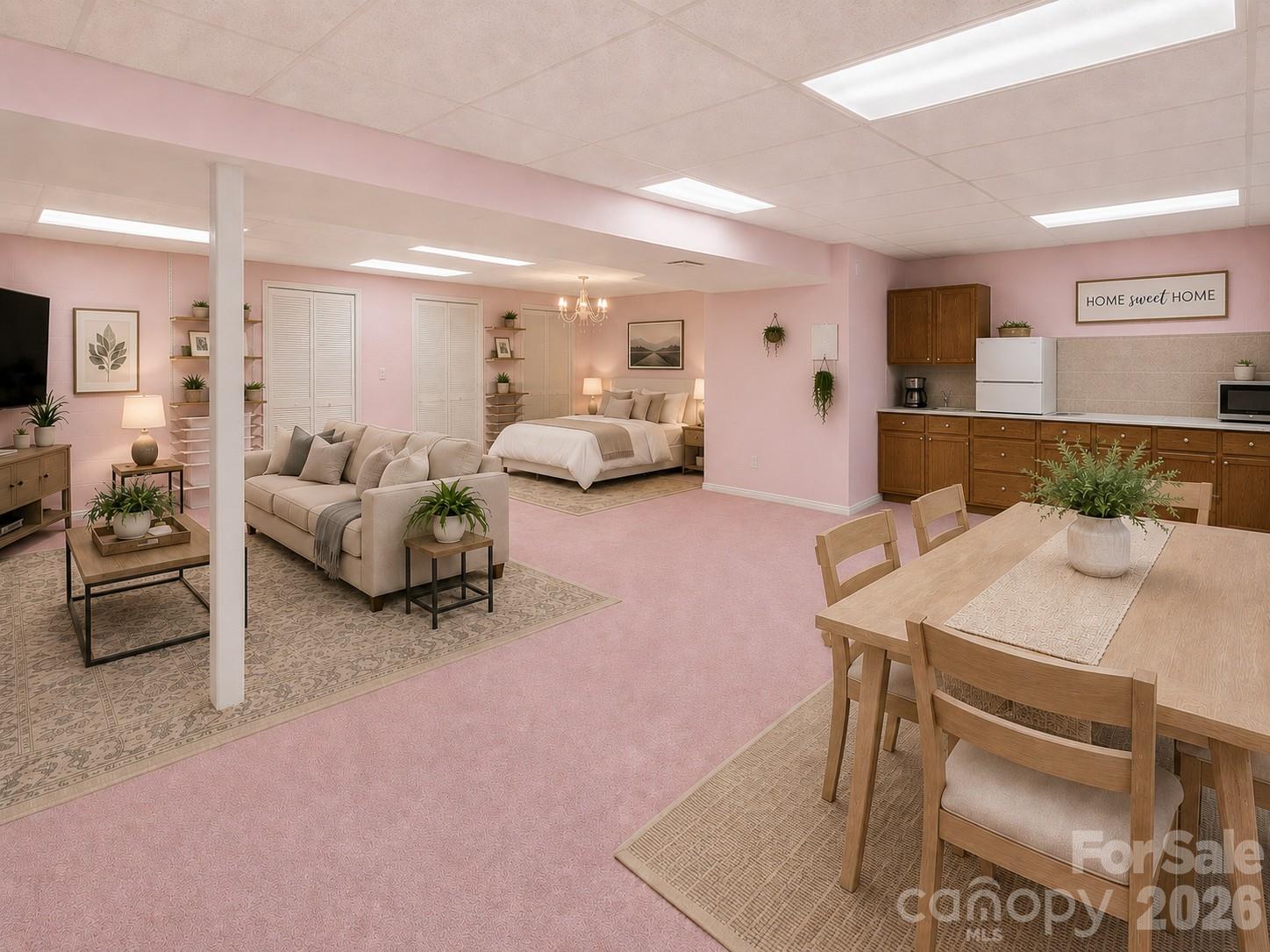 Open-plan bedroom and living area with pink walls, dining table, and kitchenette.