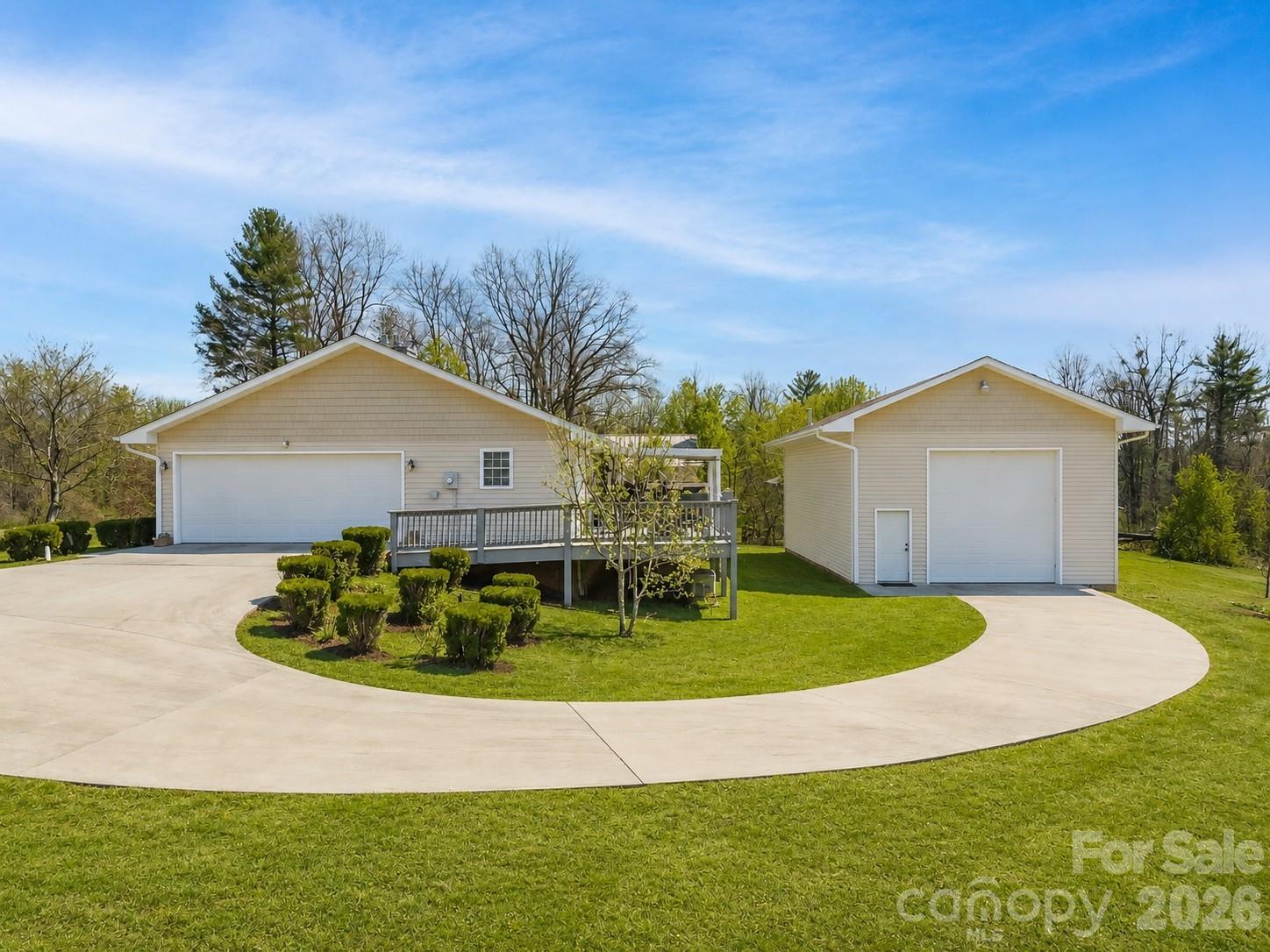Light-colored house with a raised deck and detached garage beside a curved driveway.