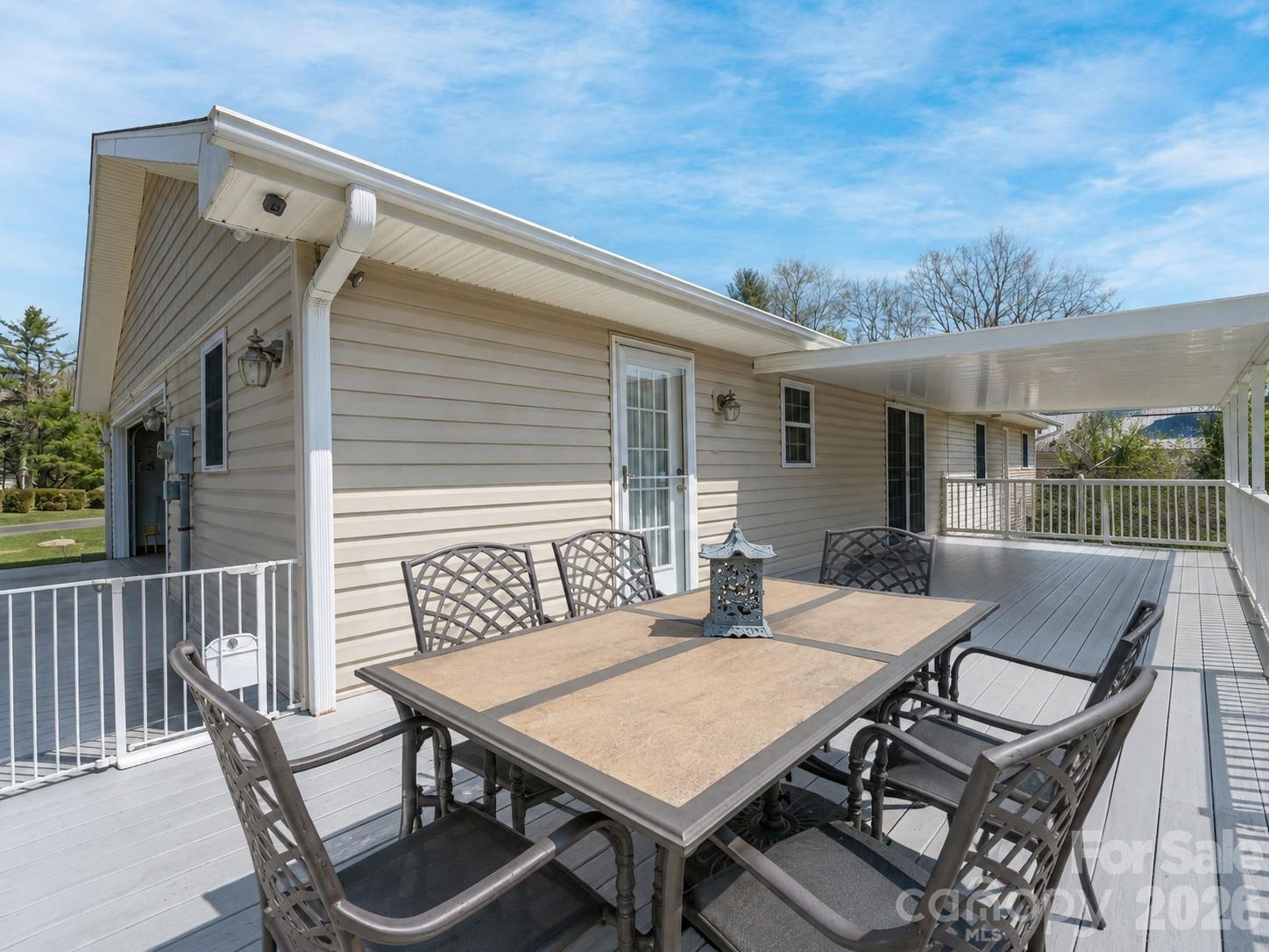 Raised deck with gray flooring, white railings, and an outdoor dining table beside the home.