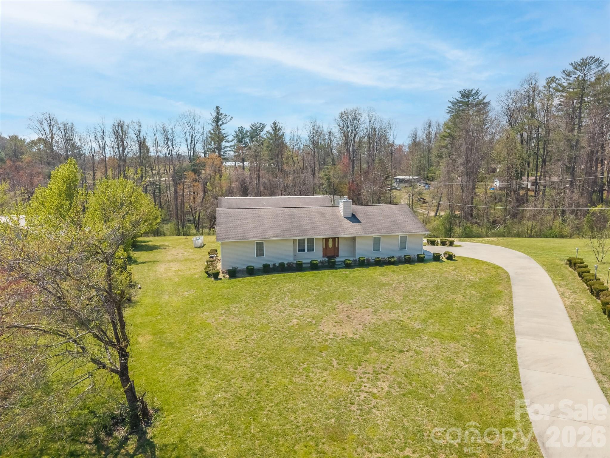 Aerial view of a single-story home with a broad lawn and curved driveway.