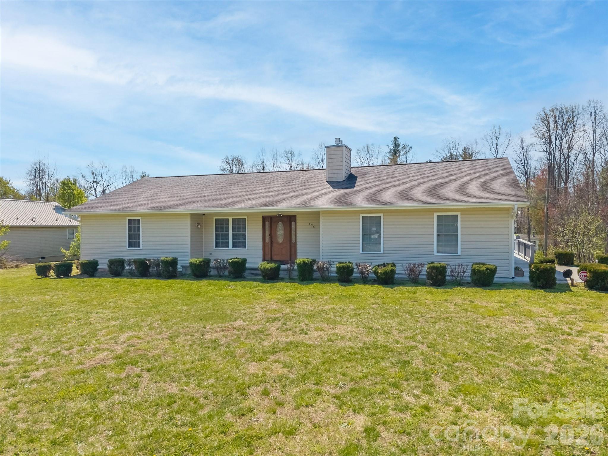 Single-story house with light siding, a broad lawn, and trimmed shrubs along the front.