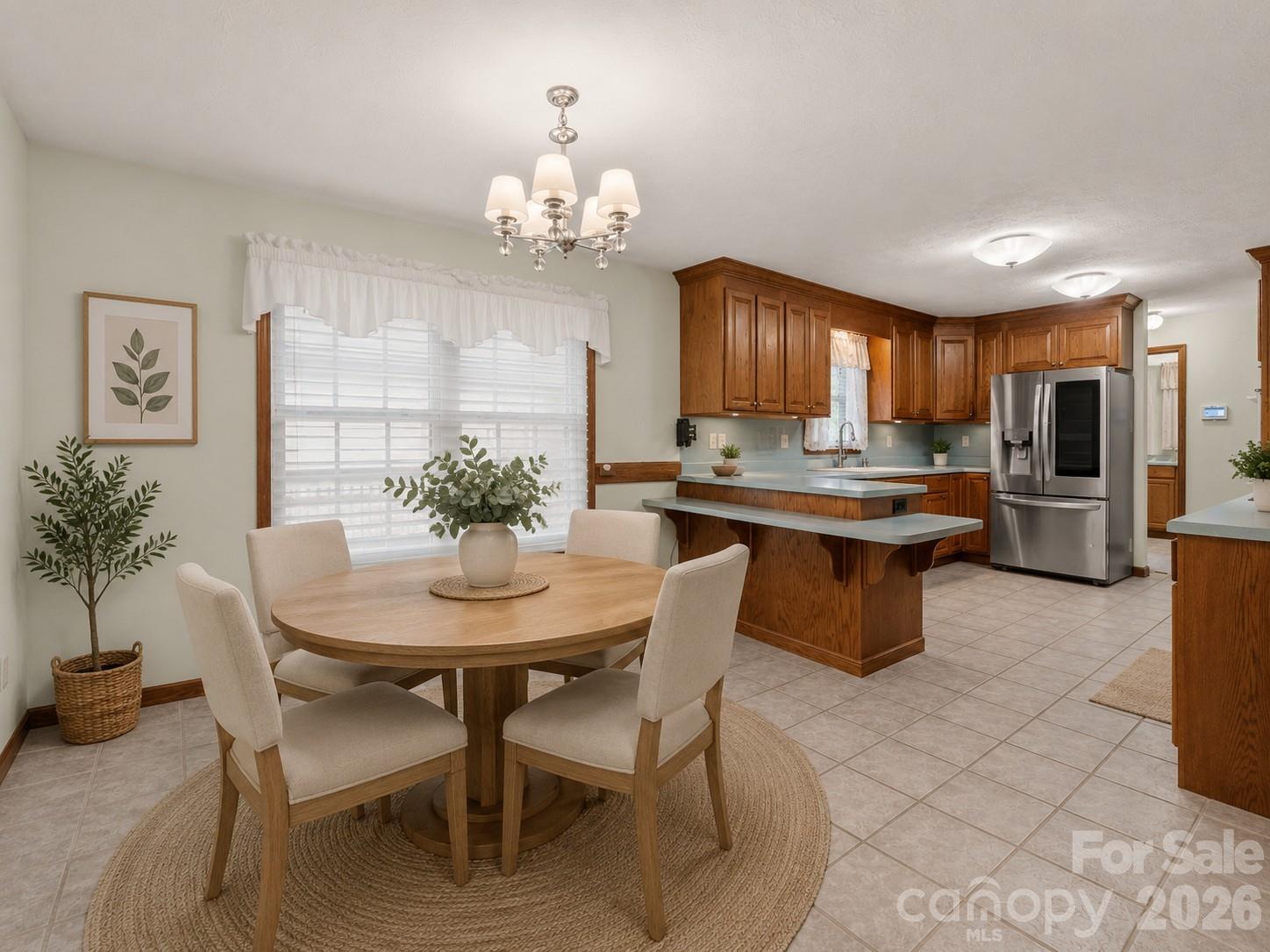 Kitchen and dining area with wood cabinets, stainless refrigerator, and a round table by the window.
