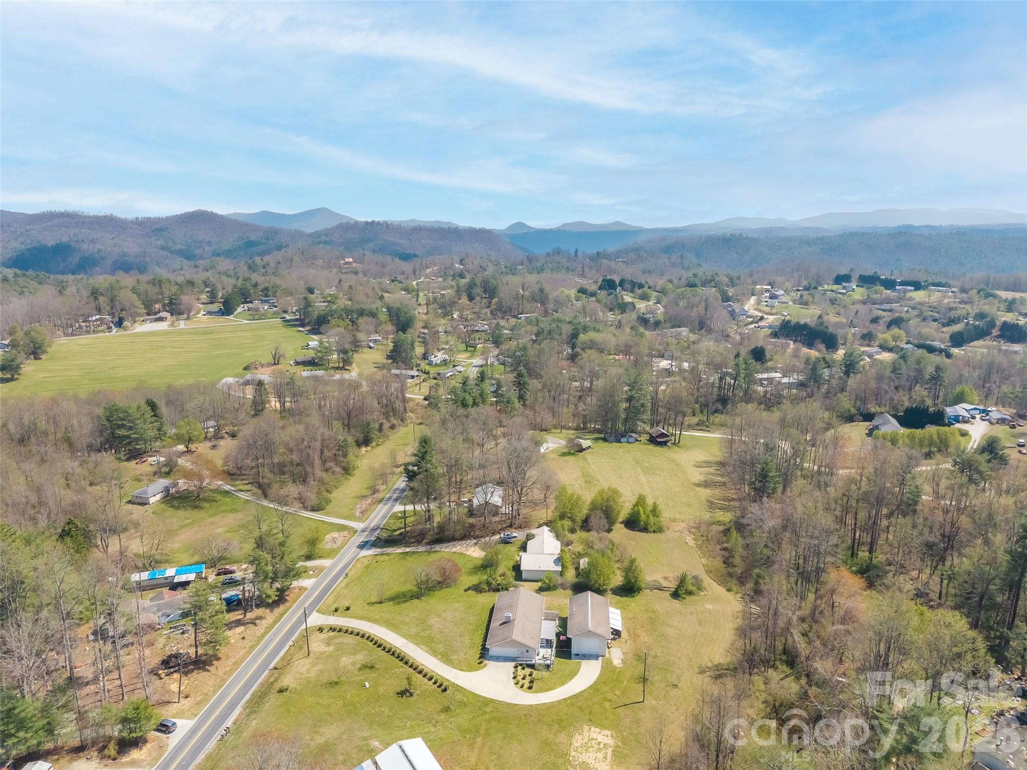 Aerial view of a home and broad lawn beside a road, with wooded hills and distant mountains.